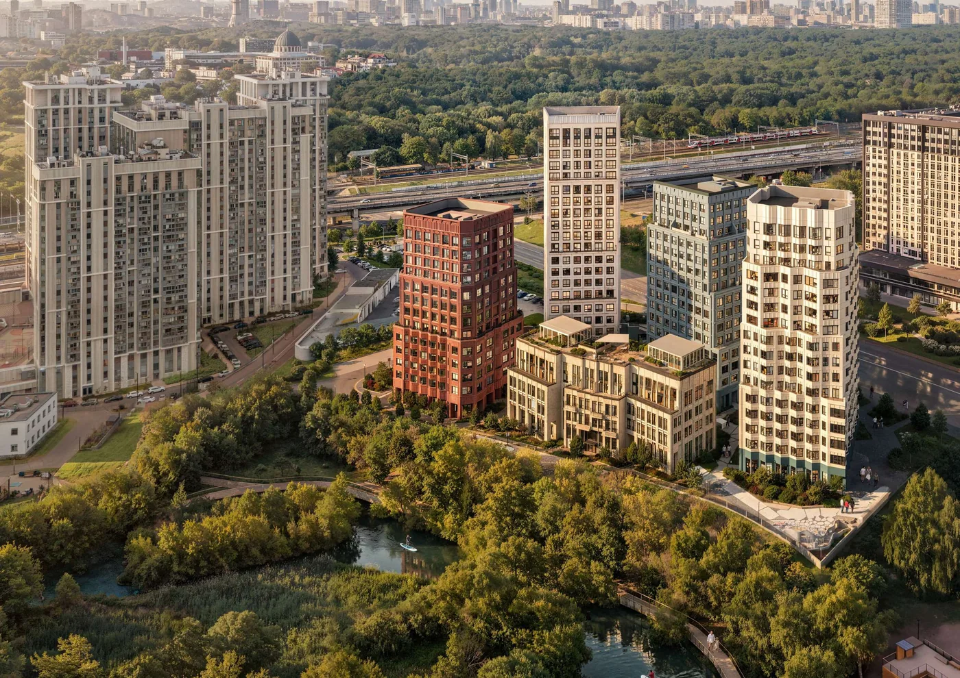 ОМ Ботанический с высоты: пять корпусов, пруд и русло Яузы, пешеходный мост, зелень поймы, скайлайн Москвы на горизонте